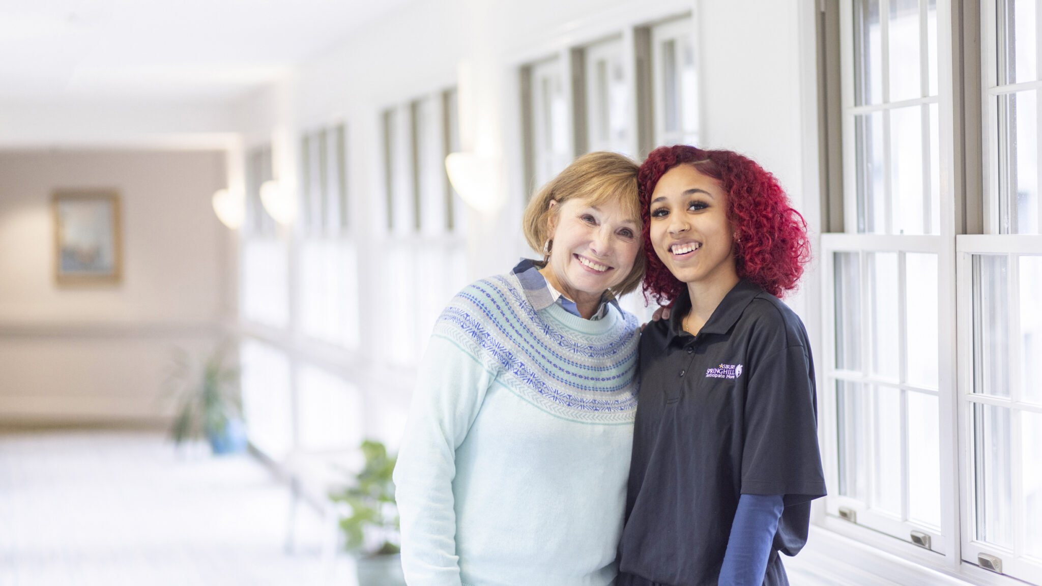 A female healthcare worker with an arm around an elderly woman's shoulder