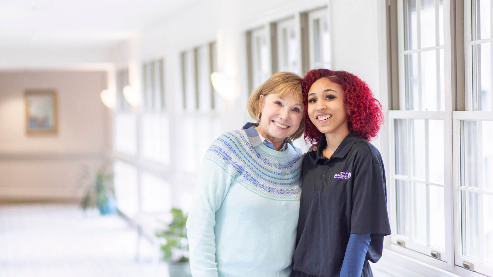 A female healthcare worker with an arm around an elderly woman's shoulder